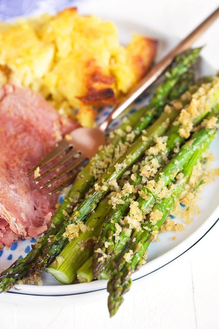Asparagus with panko on a white plate with ham and pineapple casserole.