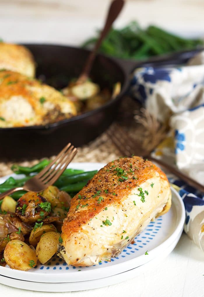 Cast iron skillet chicken on a white plate with potatoes.
