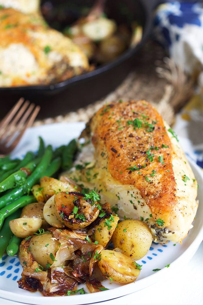 Crispy skinned cast iron skillet chicken with potatoes on a white plate.
