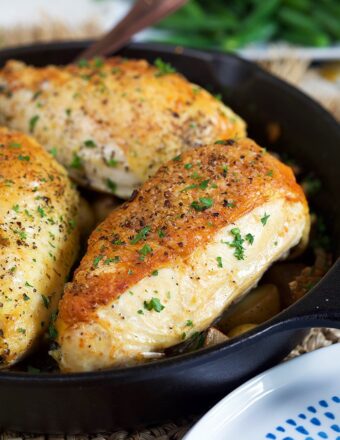 Cast Iron skillet chicken breasts in a cast iron skillet with a blue plate in the front.