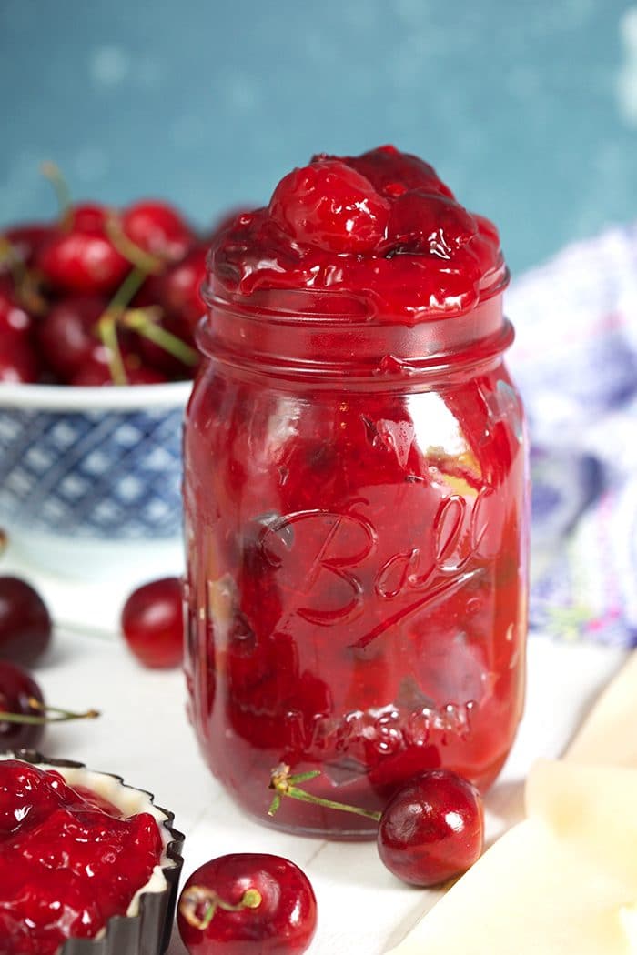 Cherry Pie Filling in a ball jar with a bowl of cherries.