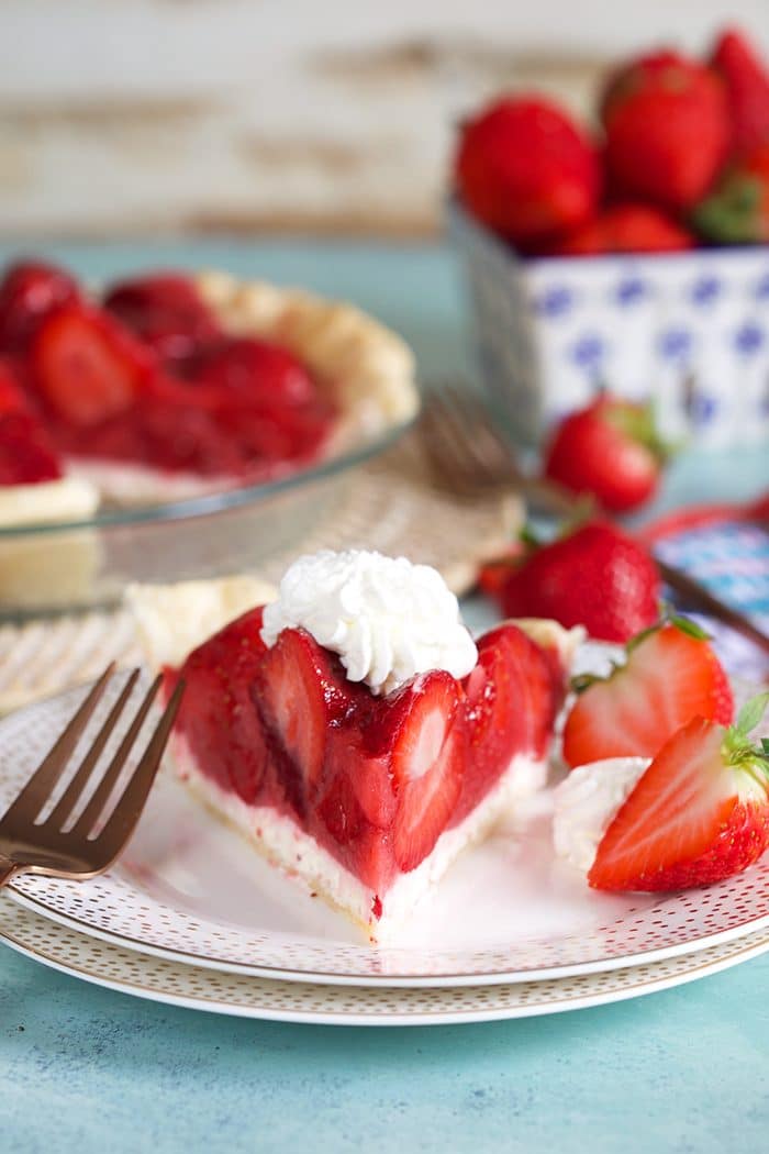 Slice of strawberry pie with whipped cream on a white plate with a fork.