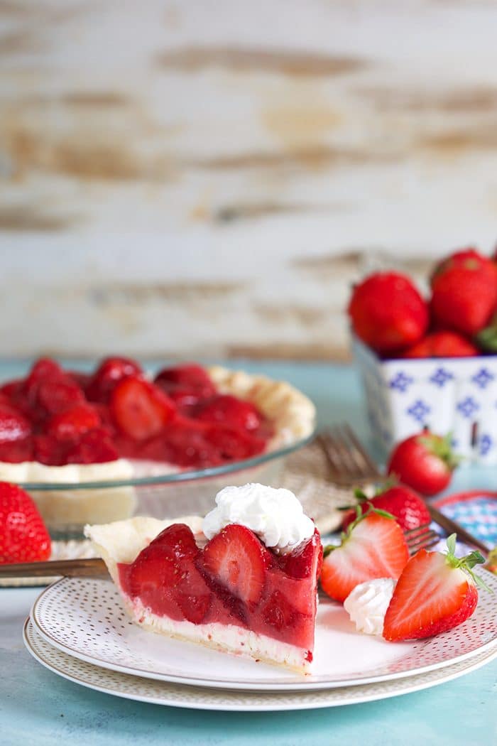 Strawberry pie on a white plate with whipped cream and berries in the background.