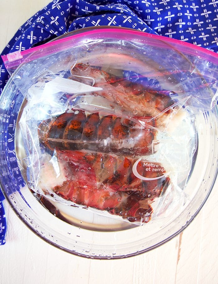 Frozen Lobster Tails in a plastic bag in a bowl of water.