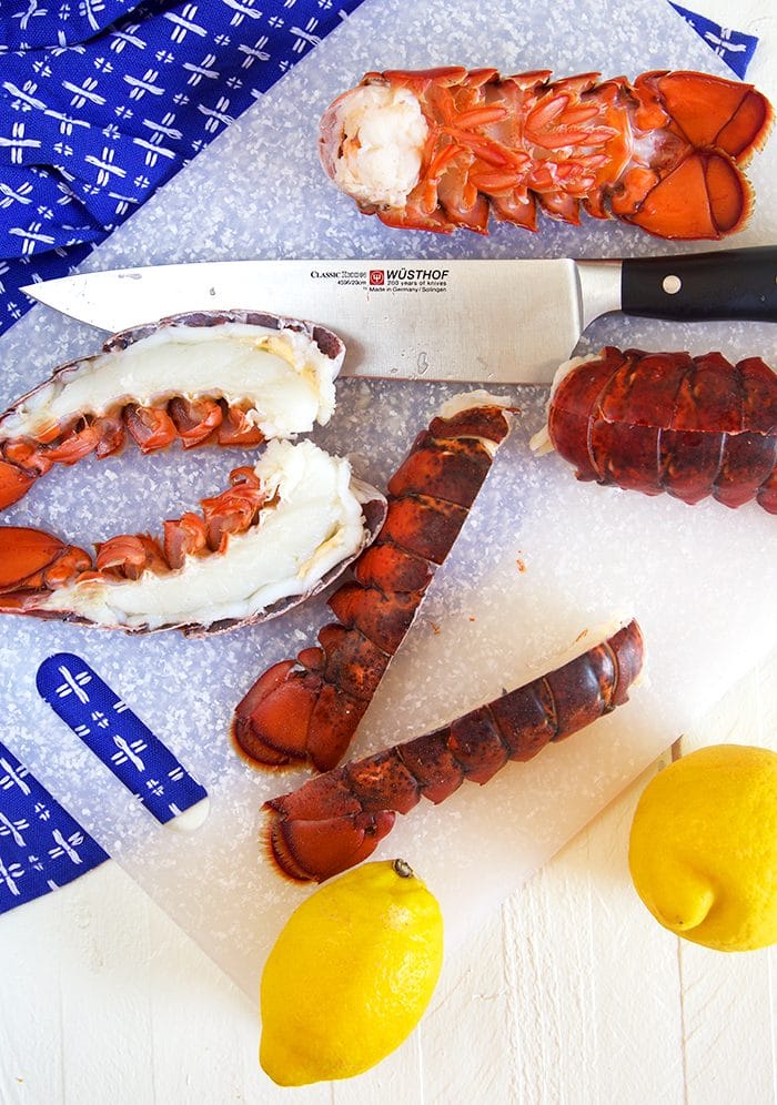 Lobster tails on a cutting board being split with a knife.