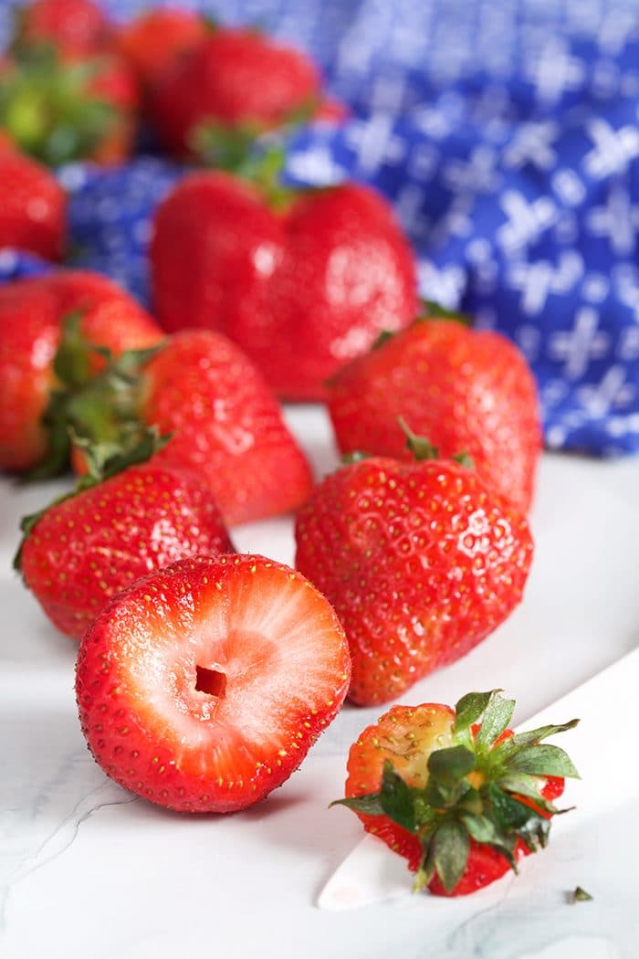 Strawberries with the tops cut off on a blue kitchen towel.