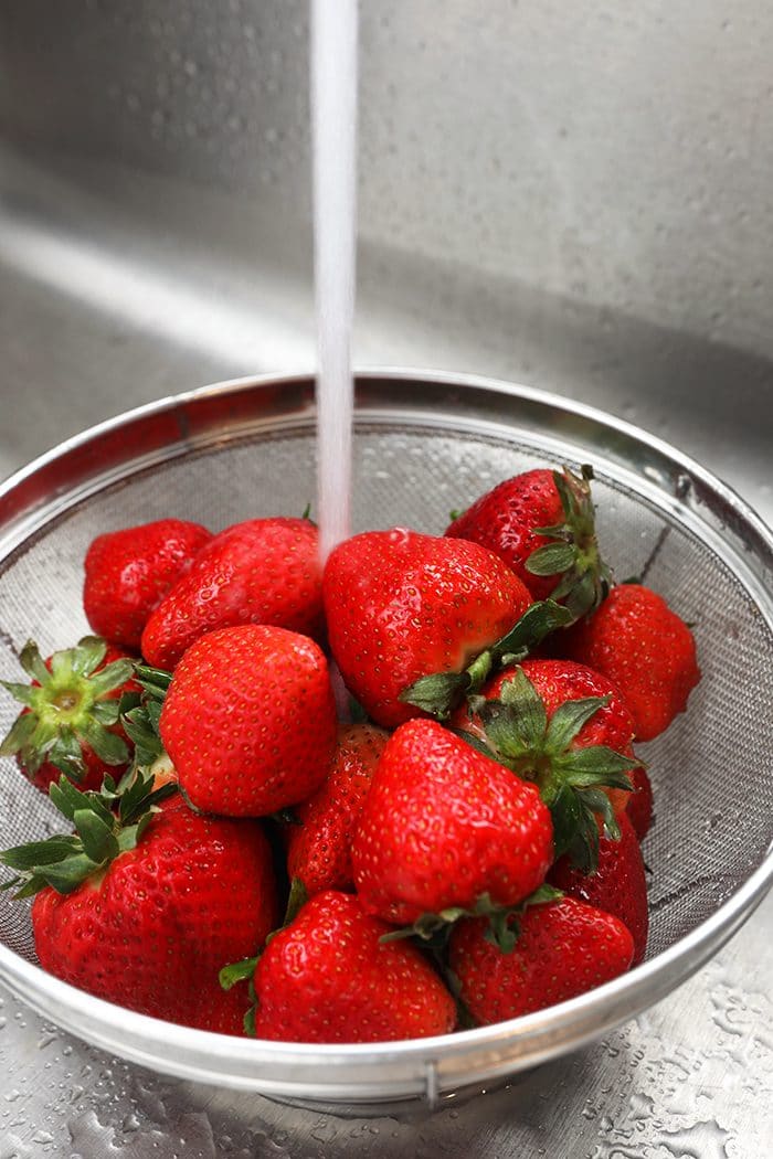 strawberries in a strainer with water running over them.