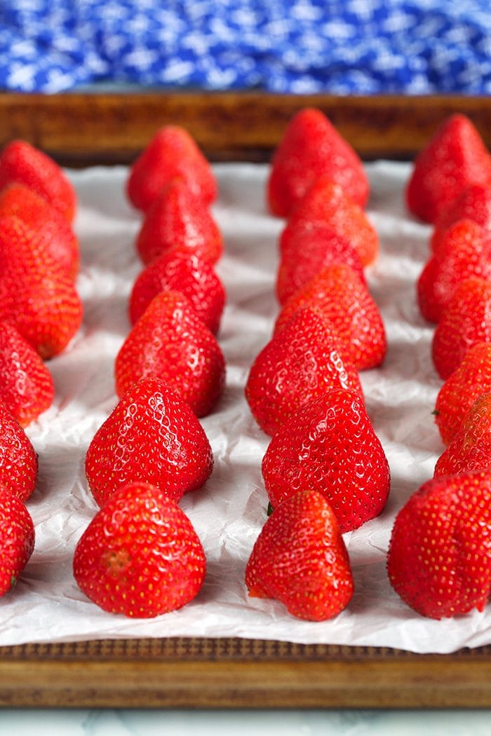 Fresh strawberries arranged on a baking sheet for freezing.