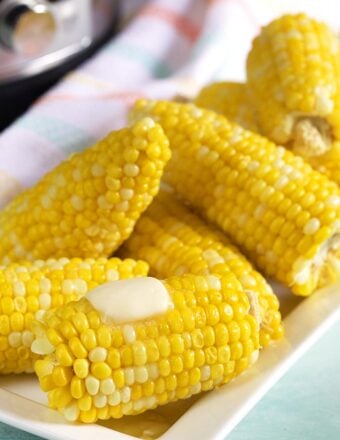 White platter with yellow corn made in the Instant Pot with a pat of butter on them.