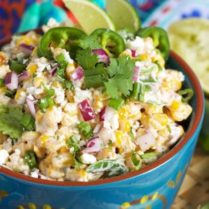 Mexican Street Corn salad in a blue bowl with two limes in them.