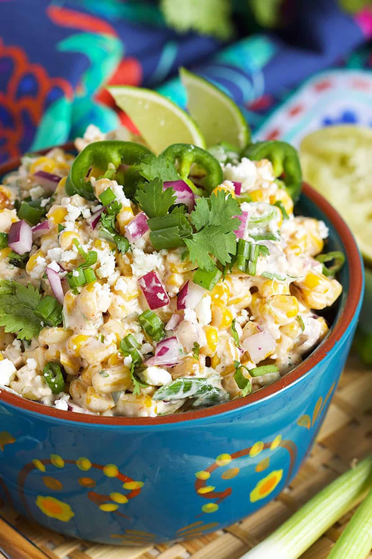 Mexican Street Corn salad in a blue bowl with two limes in them.