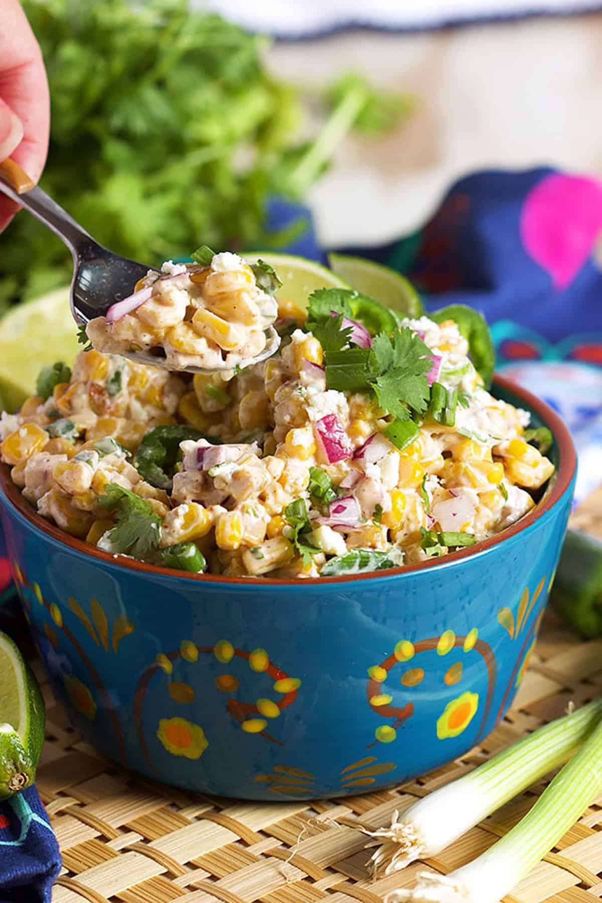 Mexican Street Corn Salad in a blue bowl with a spoon scooping out a serving of salad.