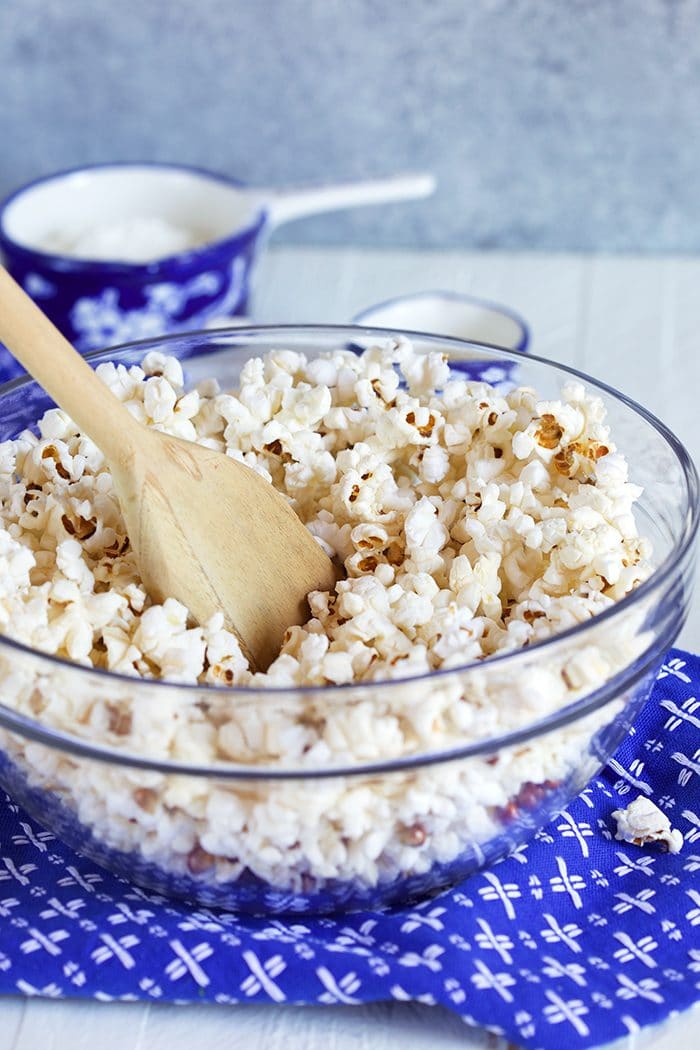 popcorn in a glass bowl being stirred with a wooden spoon.
