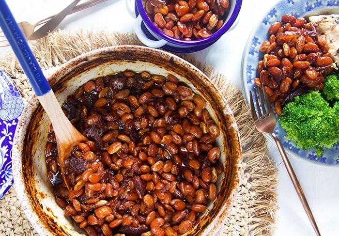overhead shot of baked beans in a blue and white pot with a blue wooden spoon.