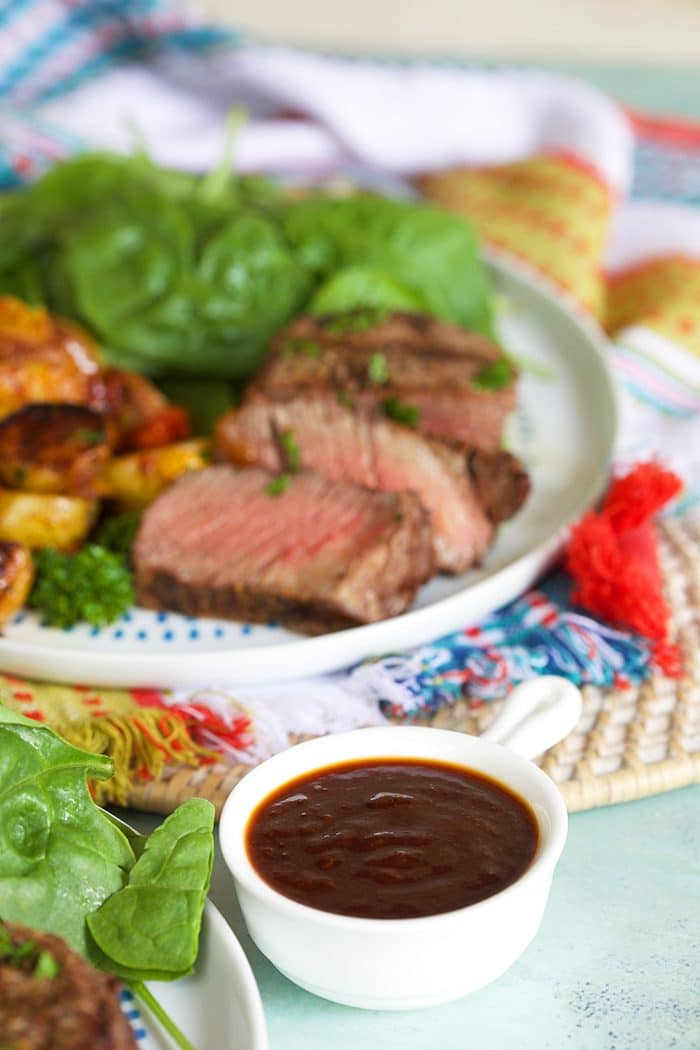 Steak sauce in a white bowl with a plate of steak and salad in the background.