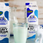 Carton of cream, glass of milk and a carton of half and half with a white cow creamer.