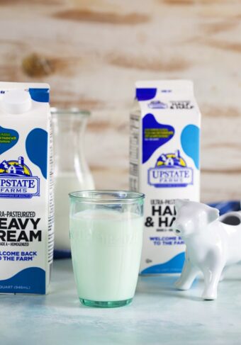 Carton of cream, glass of milk and a carton of half and half with a white cow creamer.