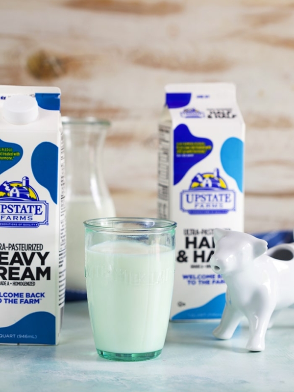 Carton of cream, glass of milk and a carton of half and half with a white cow creamer.