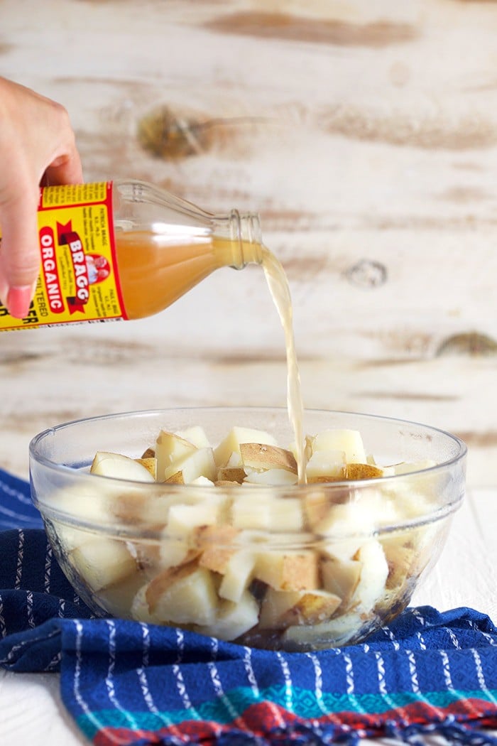 apple cider vinegar being poured over a bowl of potatoes.