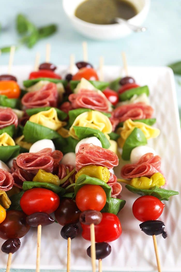 Antipasto Skewers on a white platter with pesto in a white bowl.