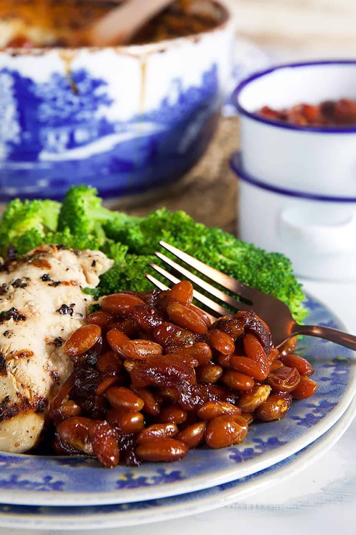 Boston Baked Beans on a blue plate with chicken and a fork.