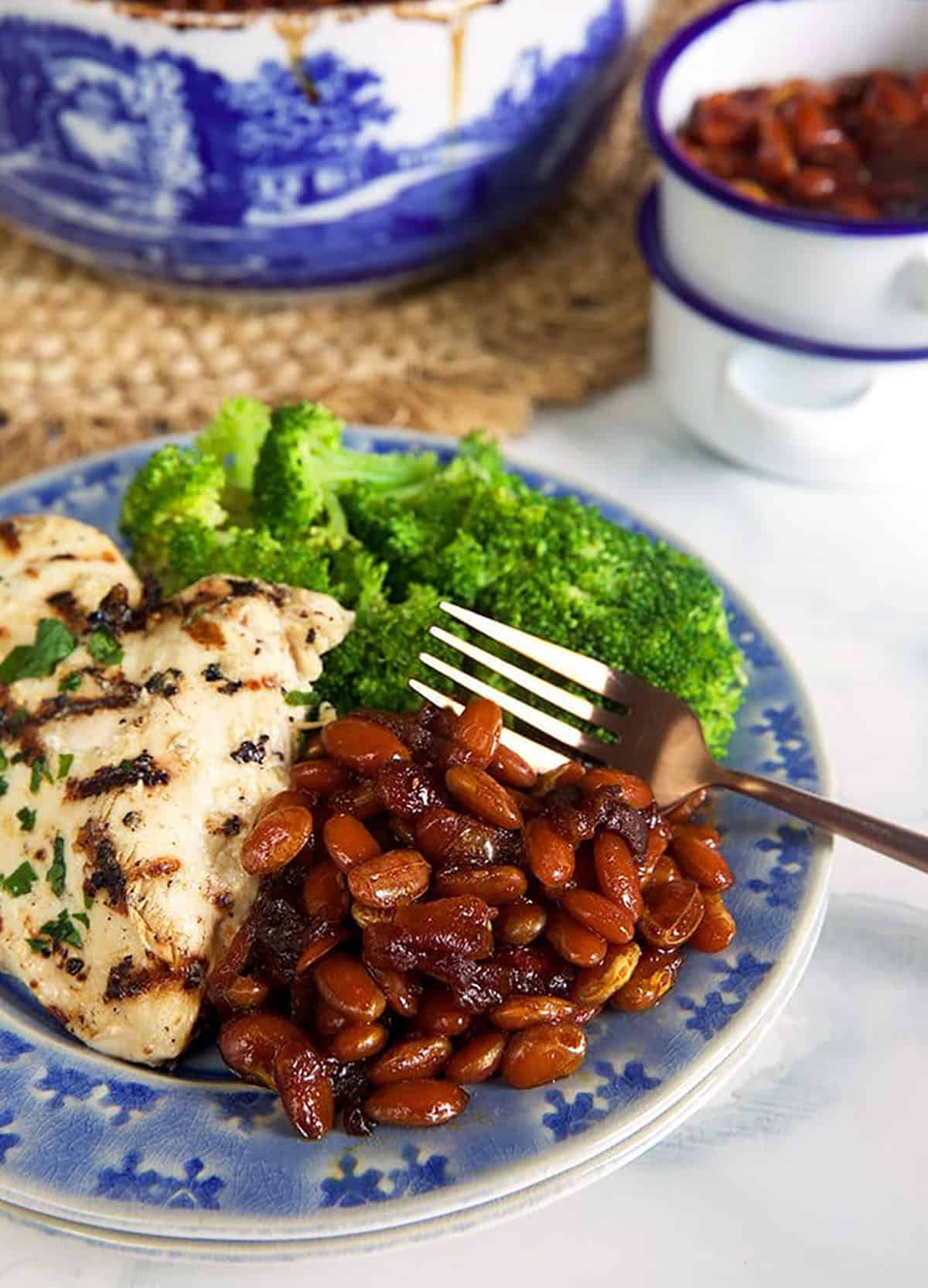 Baked beans on a blue plate with grilled chicken and broccoli.
