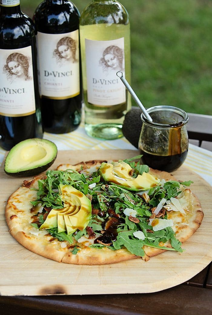pizza on a wooden pizza peel with arugula and avocado.