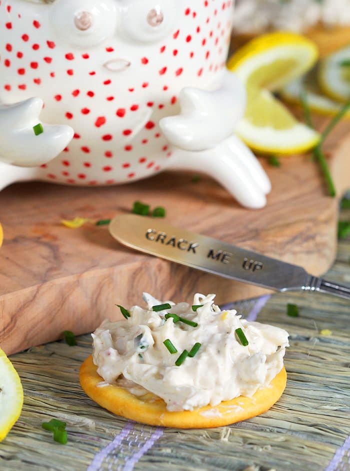 Cold Crab dip on a cracker with a spreader next to it on a wooden board.