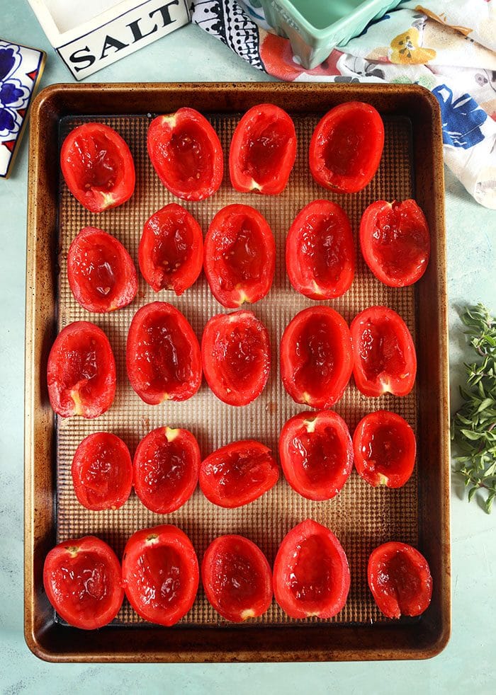 Plum tomato halves on a baking sheet in rows.