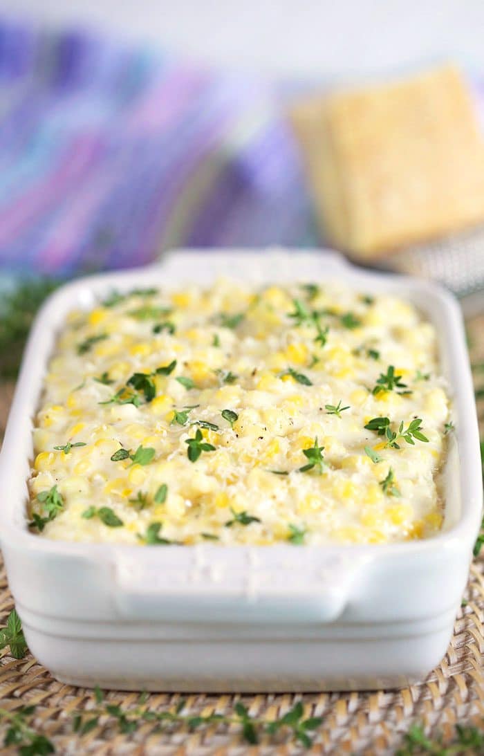 Creamed Corn in a white dish with a wedge of cheese in the back.
