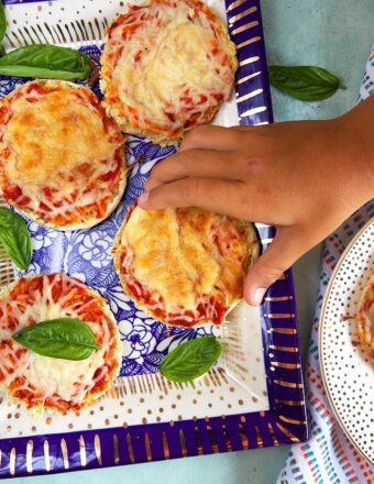 Child's hand taking an english muffin pizza off a blue and white platter.