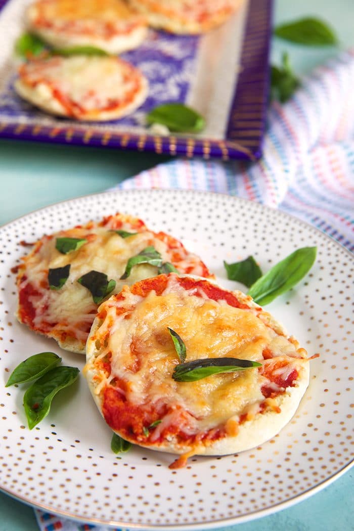 English Muffin Pizza on a white plate with gold dots and basil leaves.