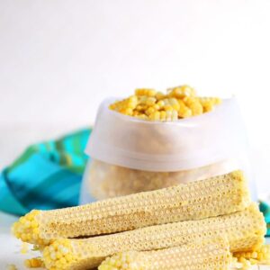 Corn off the cob in a freezer bag with cobs stacked in front.