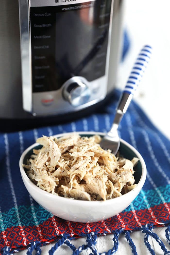 Shredded chicken breast in a white bowl with a blue and white fork.