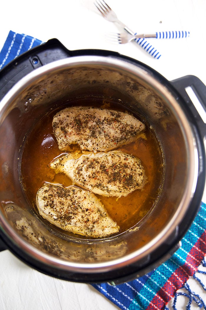 Cooked chicken breasts in stock at the bottom of an Instant Pot.