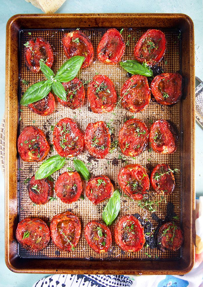Oven roasted tomatoes on a baking sheet with basil and herbs.