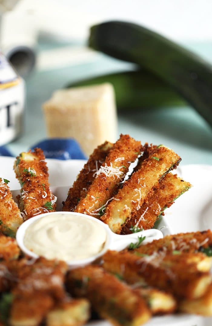 Zucchini Fries on a white platter with a wedge of parmesan and zucchini in the background.