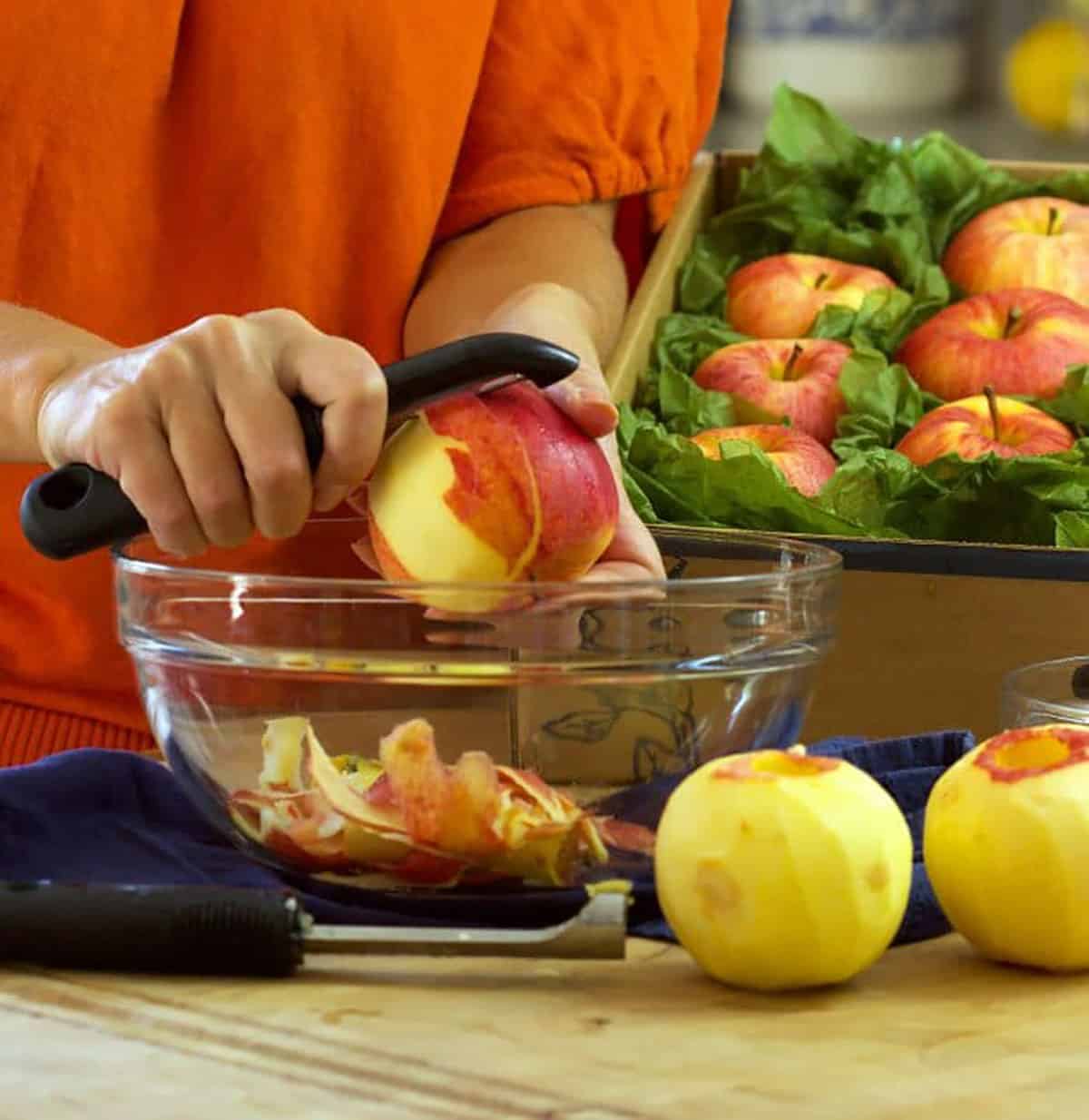 hands with a vegetable peeler removing the skin from an apple into a bowl.