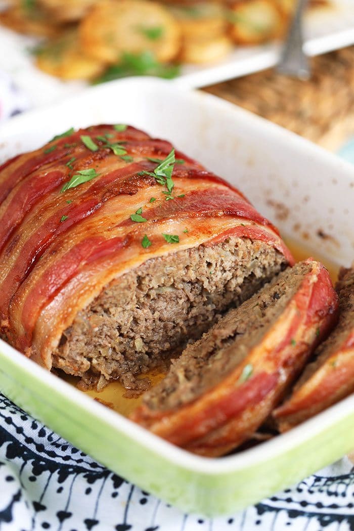 Bacon wrapped meatloaf in a green and white baking dish.