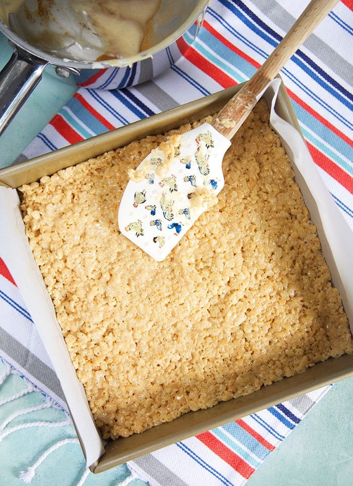 Peanut Butter Rice Krispies being pressed into a baking pan.