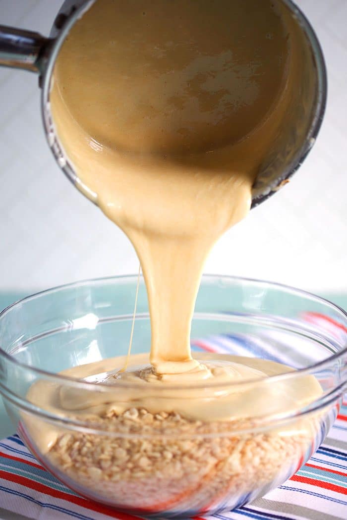 Peanut butter marshmallow sauce being poured over rice krispie cereal.