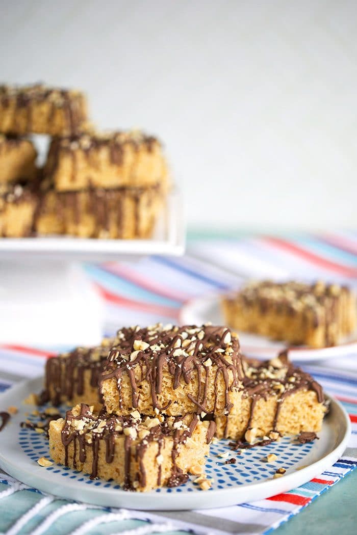 Chocolate Peanut Butter Rice Krispie treats on a plate with a cake plate in the background.
