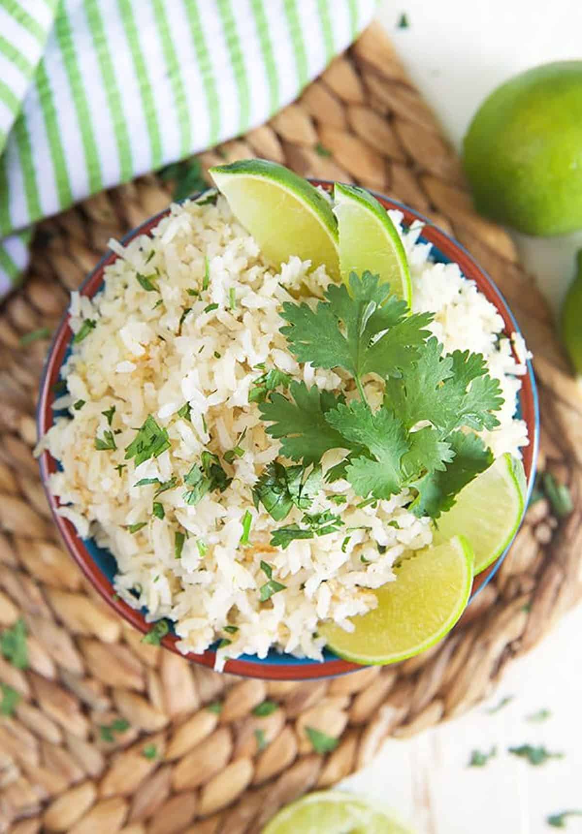 Overhead shot of cilantro lime rice with lime wedges and cilantro on a wicker place mat.
