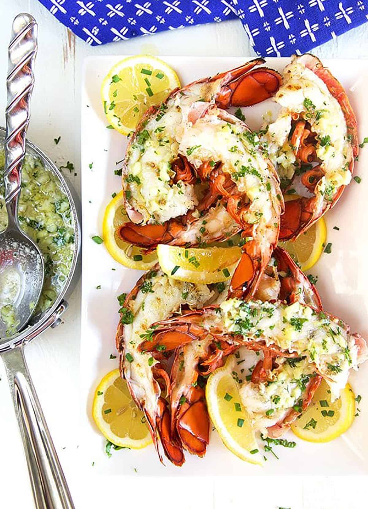 Garlic butter sauce in a saucepan next to a plate of grilled lobster tails.