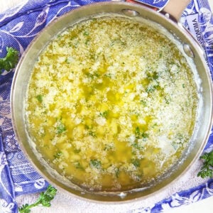 Garlic butter sauce in a saucepan on a blue and white potholder.