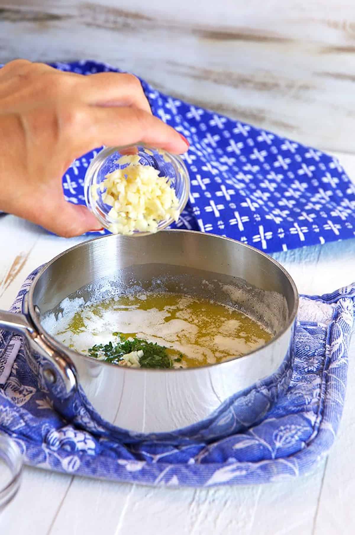 Garlic being poured into a saucepan of melted butter.