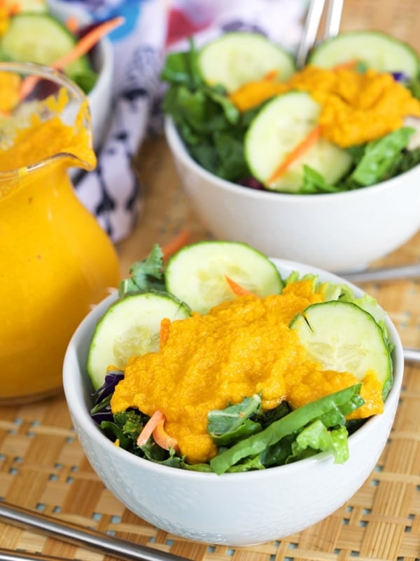 Green salad in a white bowl with carrot ginger dressing.