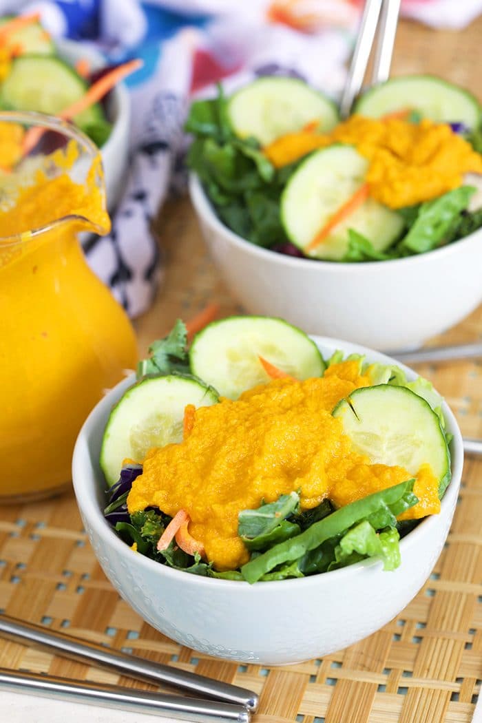 Green salad in a white bowl with carrot ginger dressing.