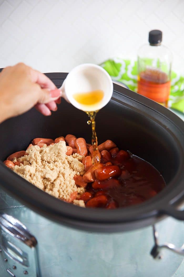 Bourbon being poured into a crockpot with little smokies.