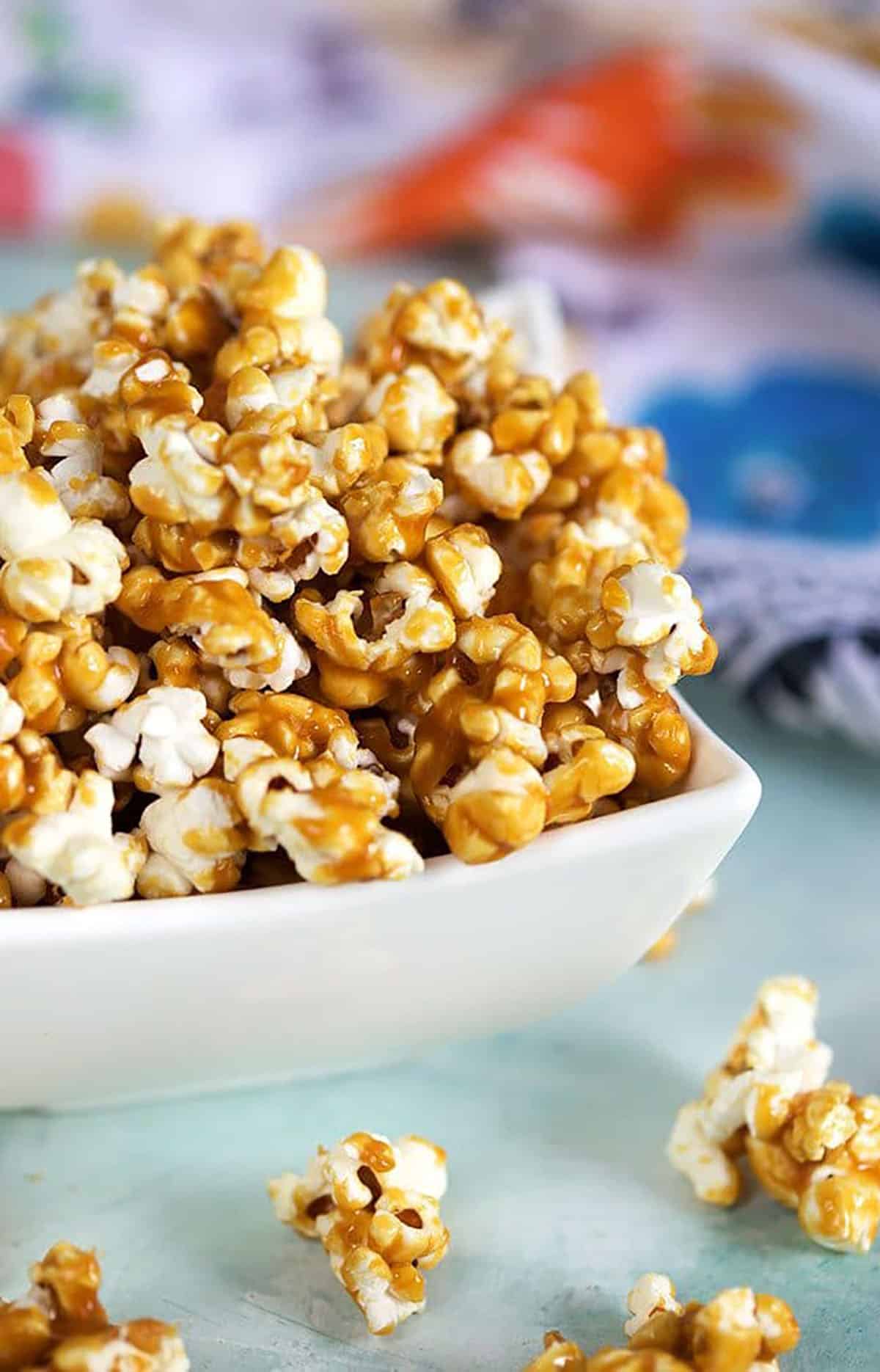Close up of caramel corn in a white bowl on a blue background.